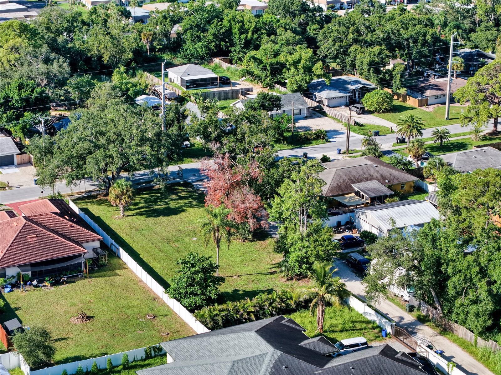 Aerial view of a fenced grassy lot surrounded by homes and mature trees.