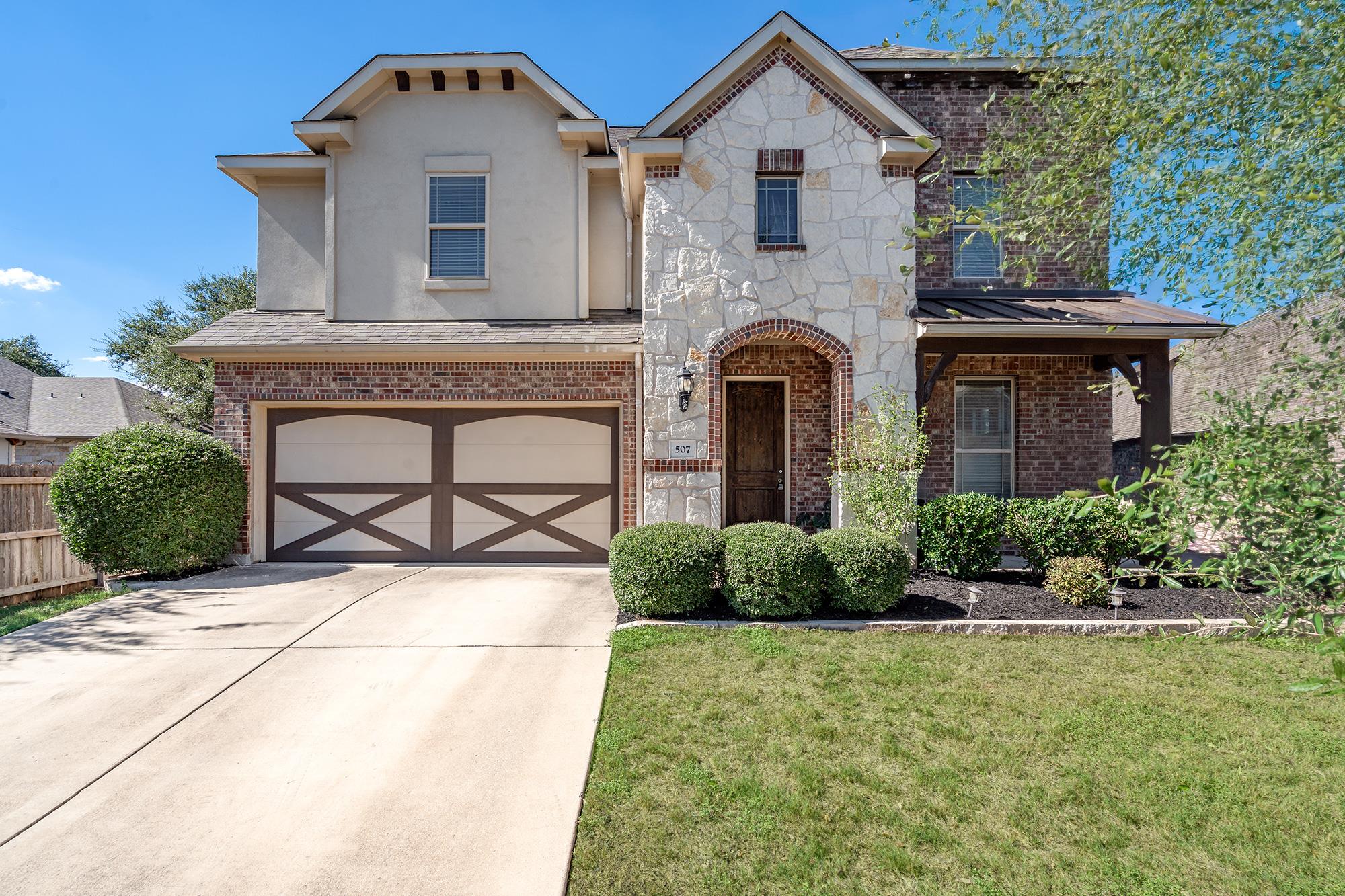 Two-story stone and brick home with a double garage, covered porch, and landscaped front yard.