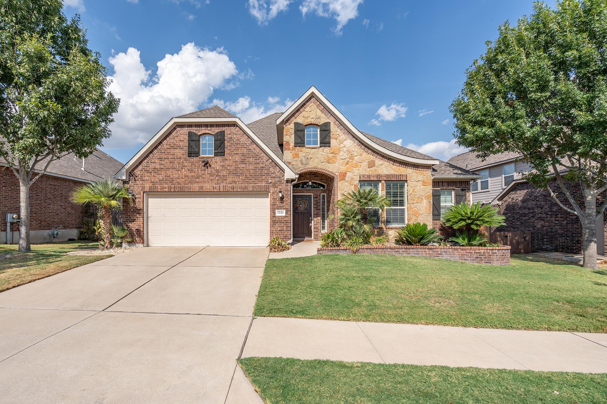 Two-story brick and stone home with a two-car garage, landscaped front yard, and broad driveway.