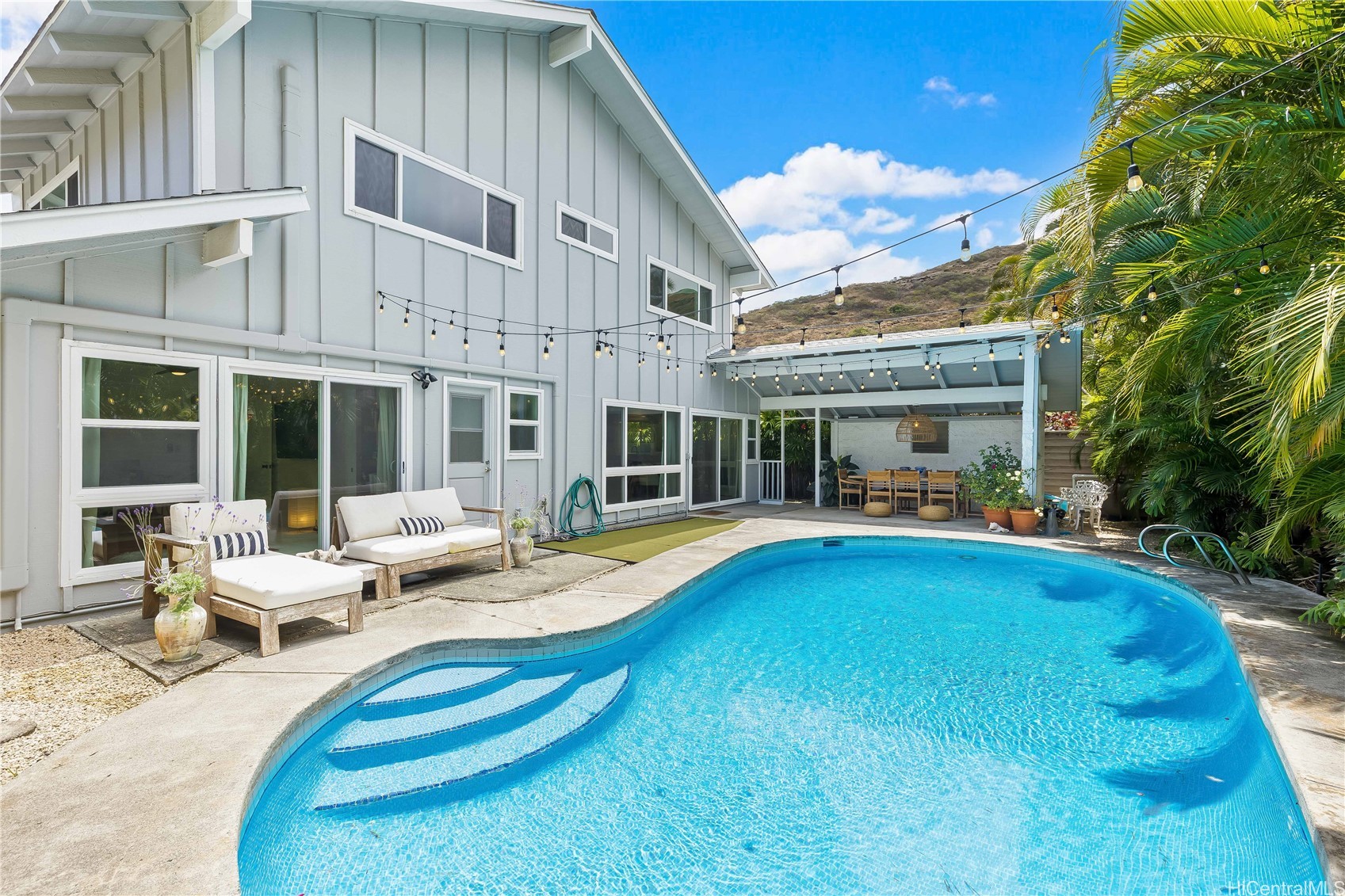 Home backyard with a curved swimming pool, lounge seating, and a covered outdoor dining area.