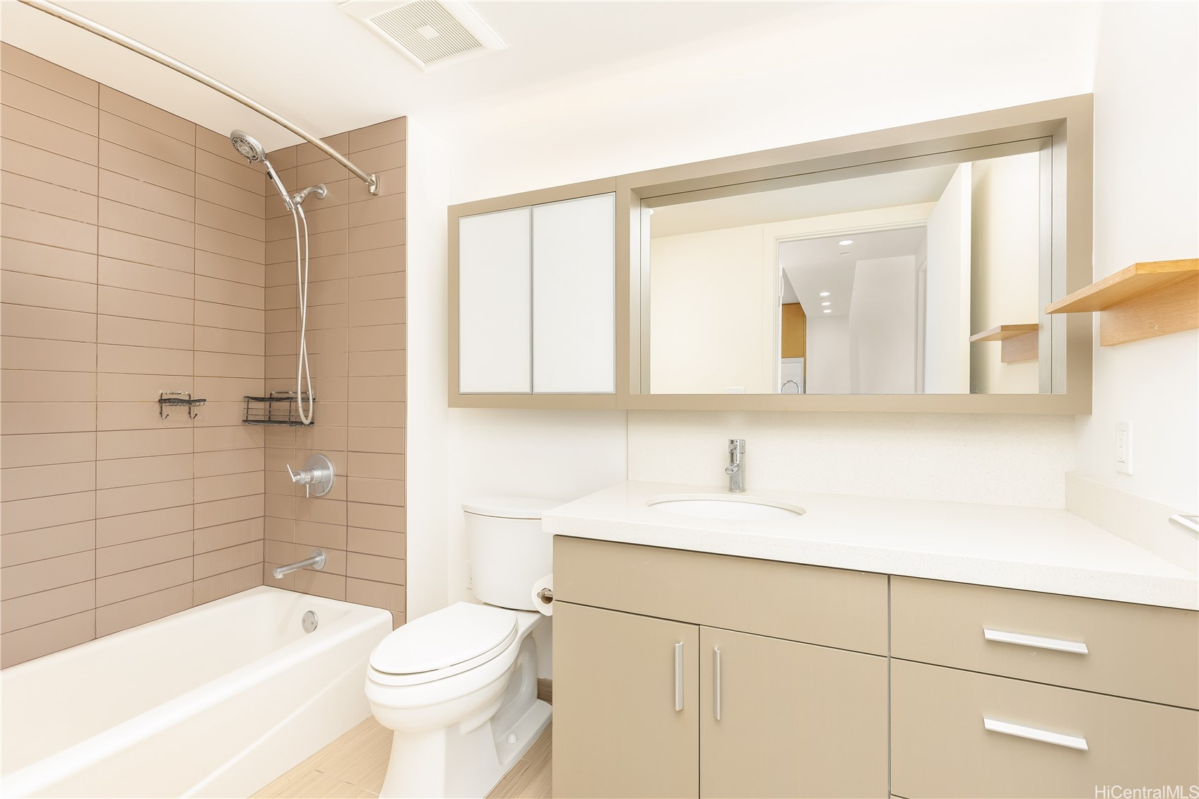 Bathroom with a tiled tub and shower, toilet, and beige vanity with a wide mirrored cabinet.