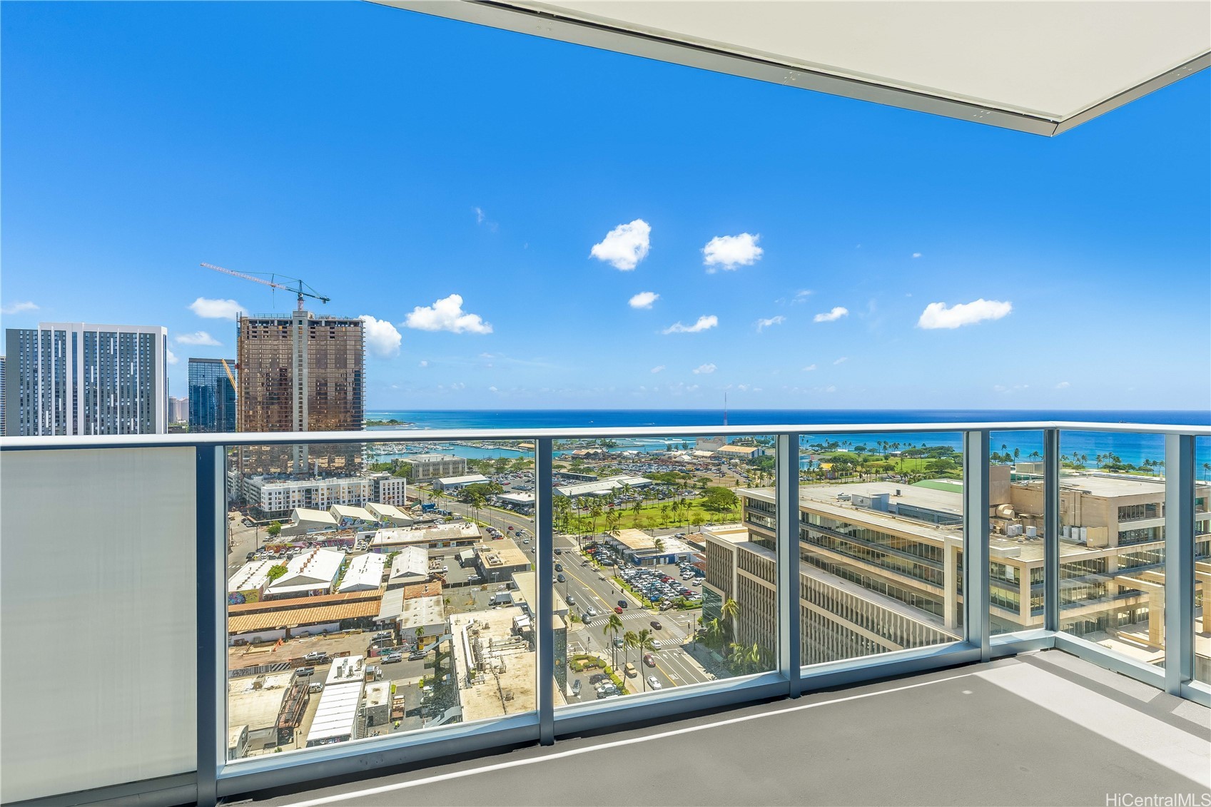 High-rise balcony overlooking the Pacific Ocean and Honolulu cityscape, with a glass railing and blue sky.