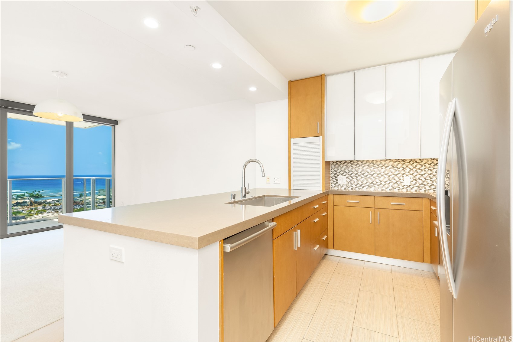 Modern kitchen with a stone island and light wood cabinets, overlooking the ocean through sliding glass doors.