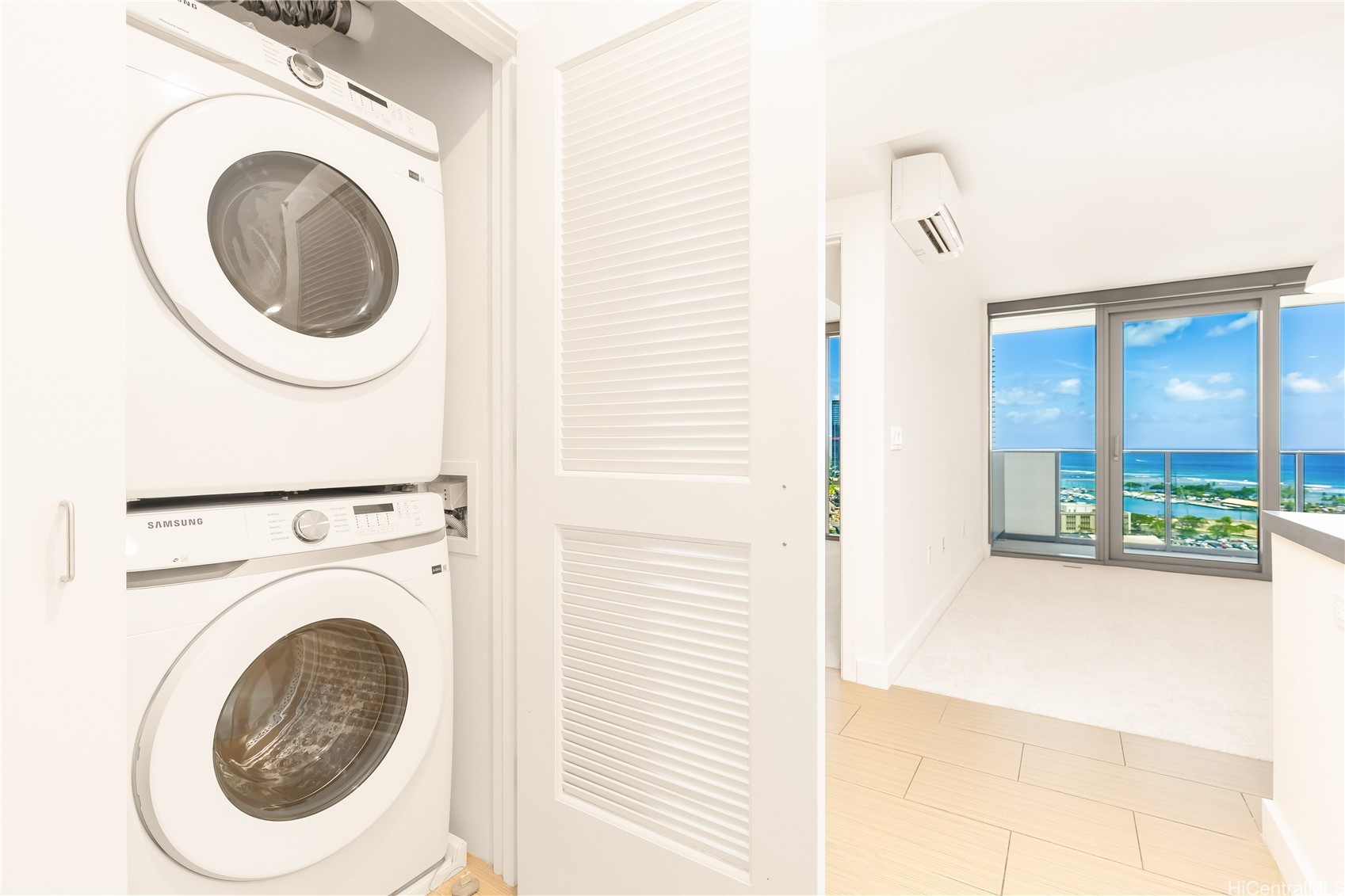 Stacked washer and dryer beside an empty room with sliding doors overlooking the ocean.