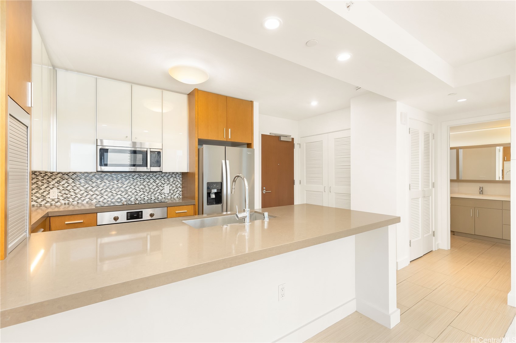 Condo kitchen with a large stone island, stainless steel appliances, and a rounded mosaic backsplash.