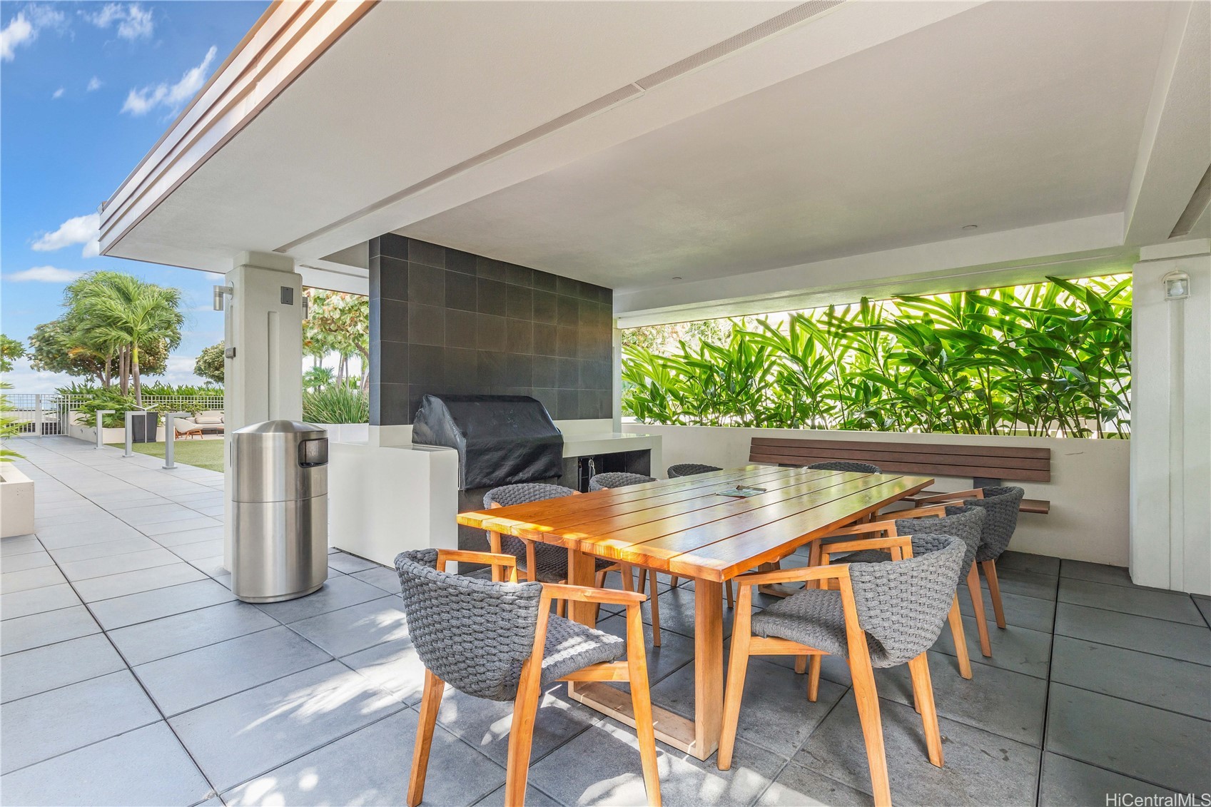 Covered outdoor dining area with a long wooden table, woven chairs, and built-in grill.