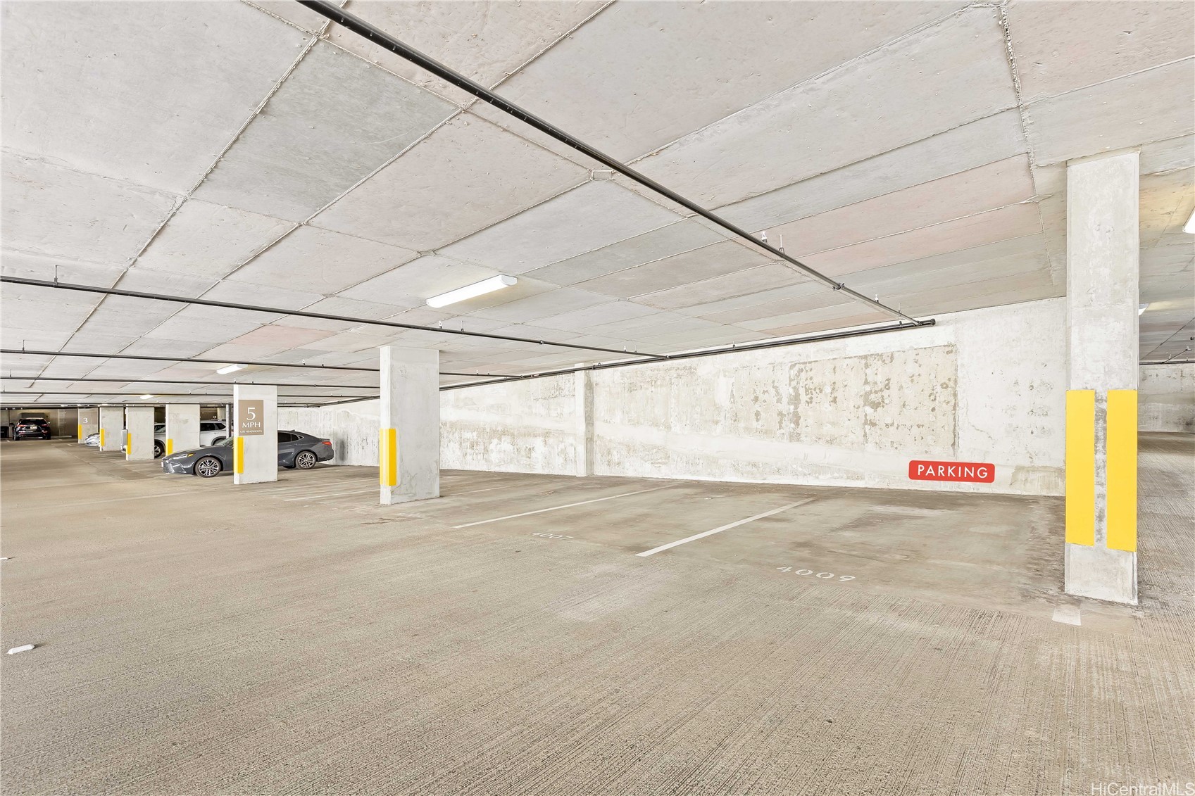 Concrete parking garage with marked spaces, yellow column guards, and a 5 MPH sign.