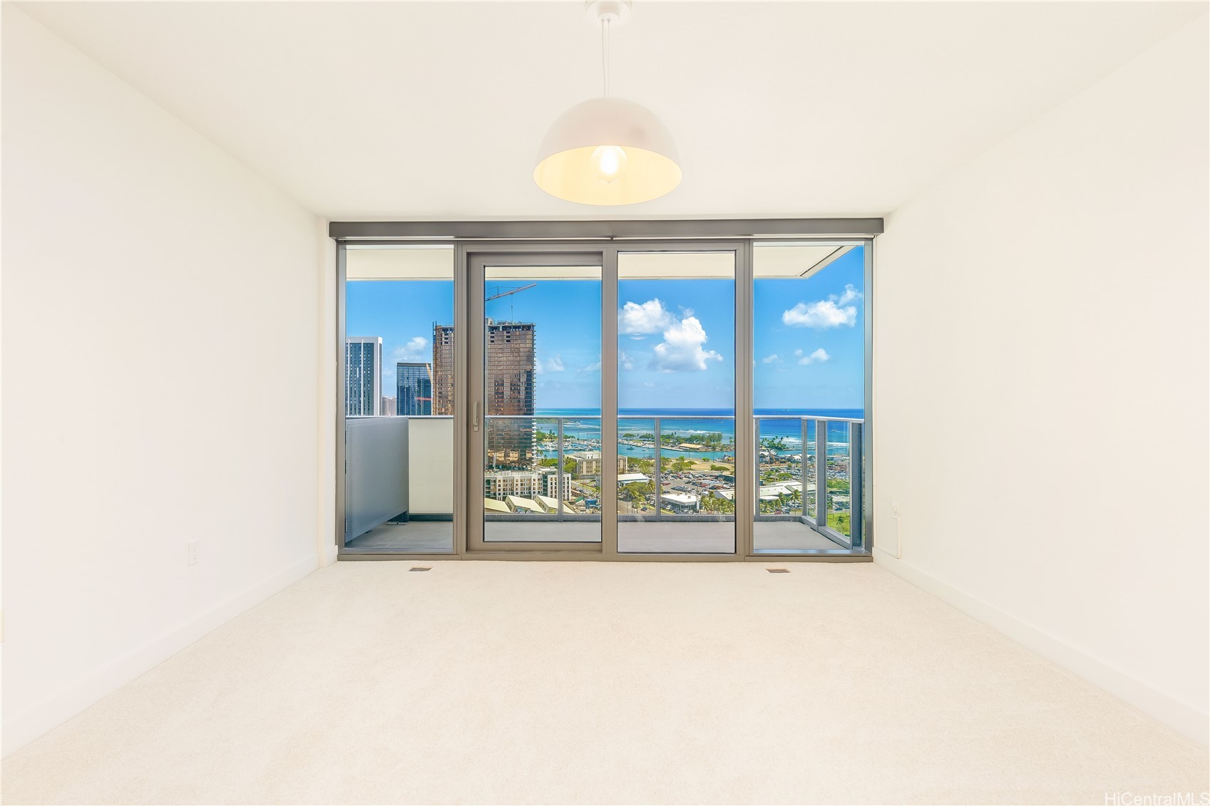 Vacant carpeted room with sliding glass doors and balcony overlooking Honolulu and the ocean.