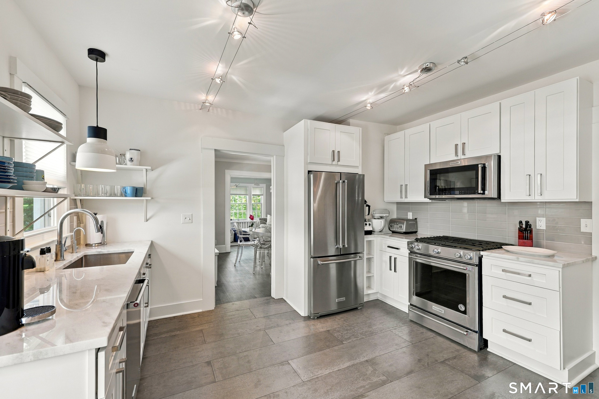 Bright white kitchen with stainless steel appliances, quartz counters, and open shelving.