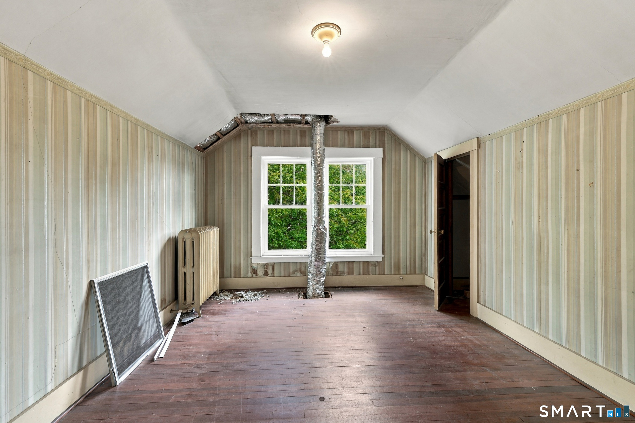Vacant attic room with striped wallpaper, sloped ceiling, exposed ductwork, and worn wood floors.
