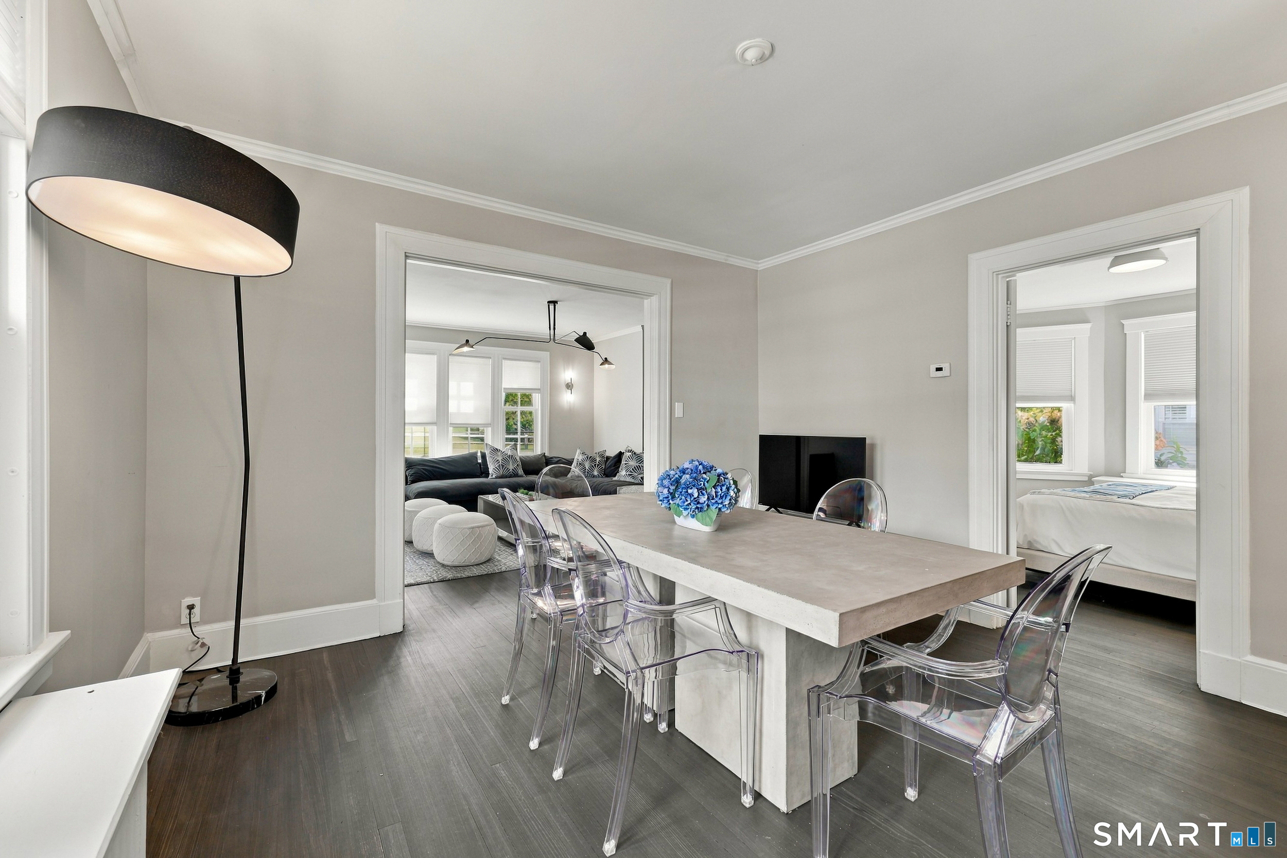 Staged dining room with a stone table and clear chairs, opening onto a living room and bedroom.