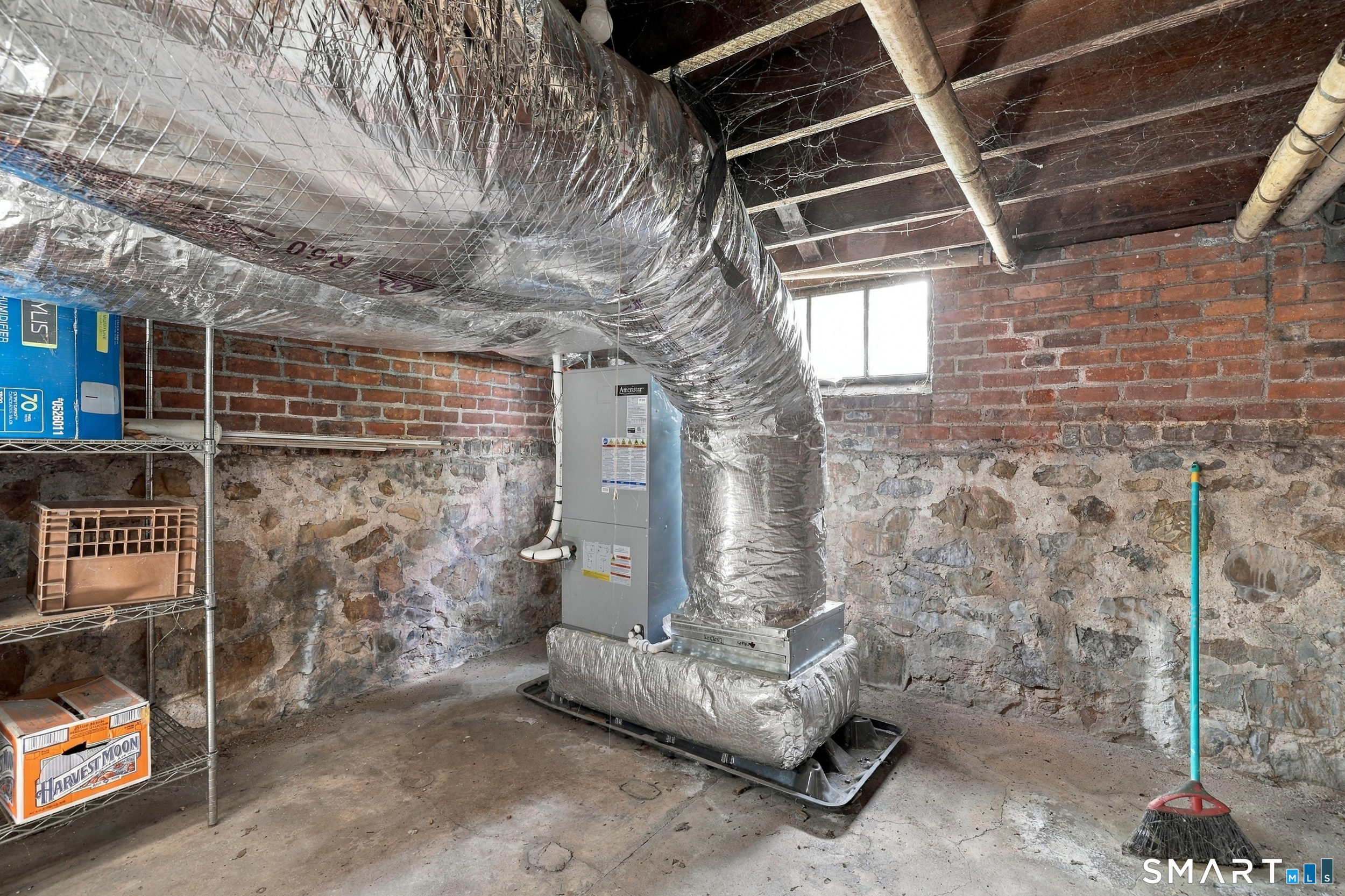 Basement mechanical room with large insulated HVAC ductwork and exposed stone and brick walls.