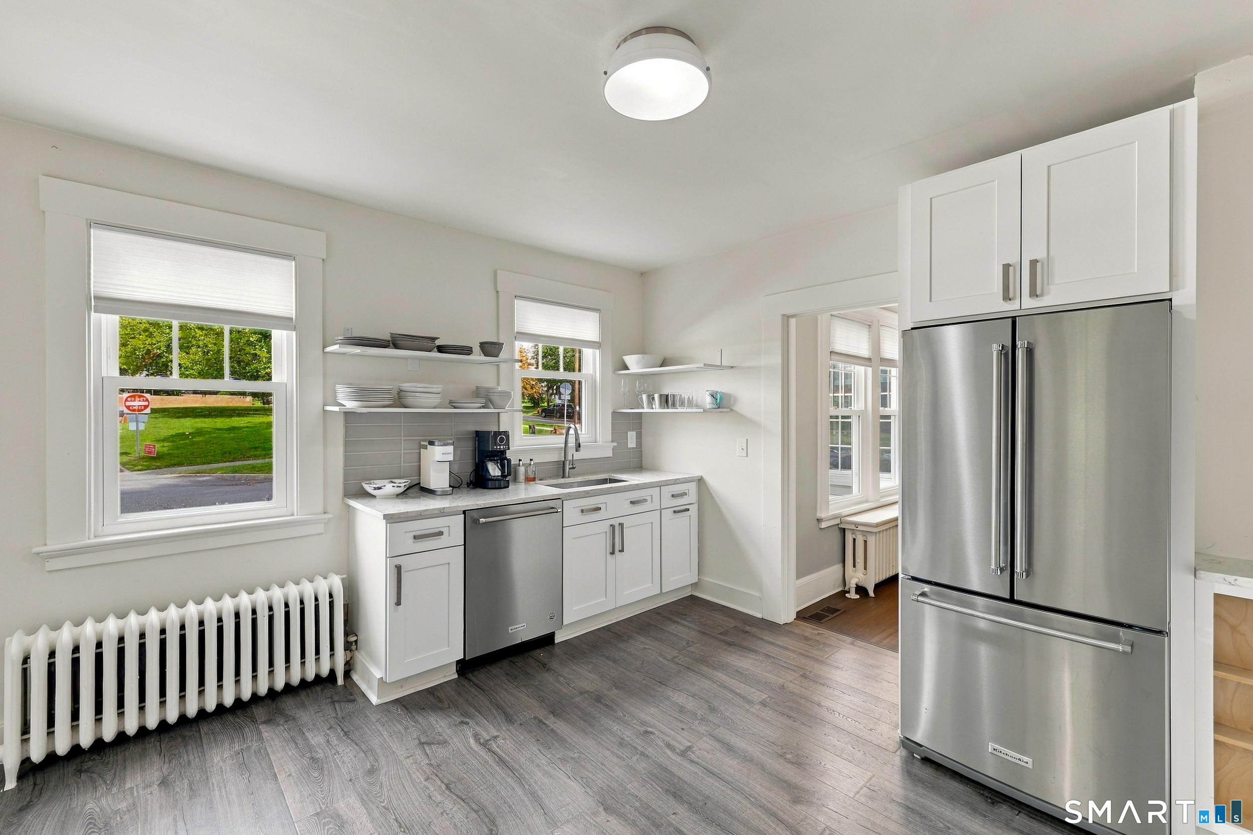 Kitchen with white cabinetry, stainless steel appliances, open shelves, and gray wood-look flooring.