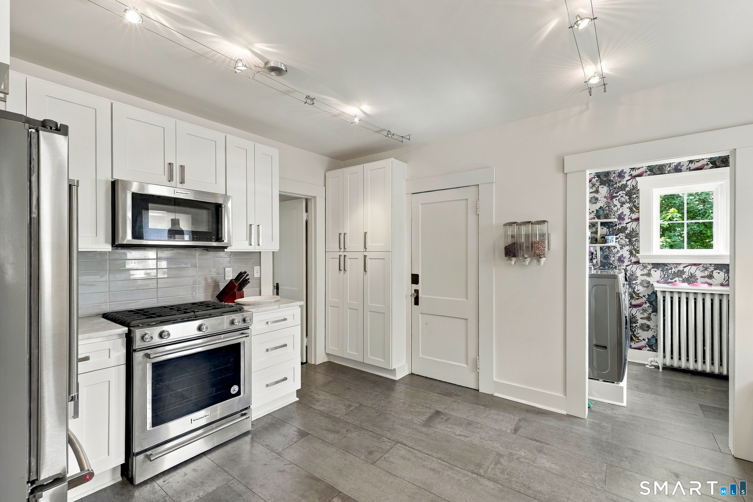 Kitchen with white cabinetry, stainless steel appliances, gray tile floors, and a doorway to a floral-wallpapered room.