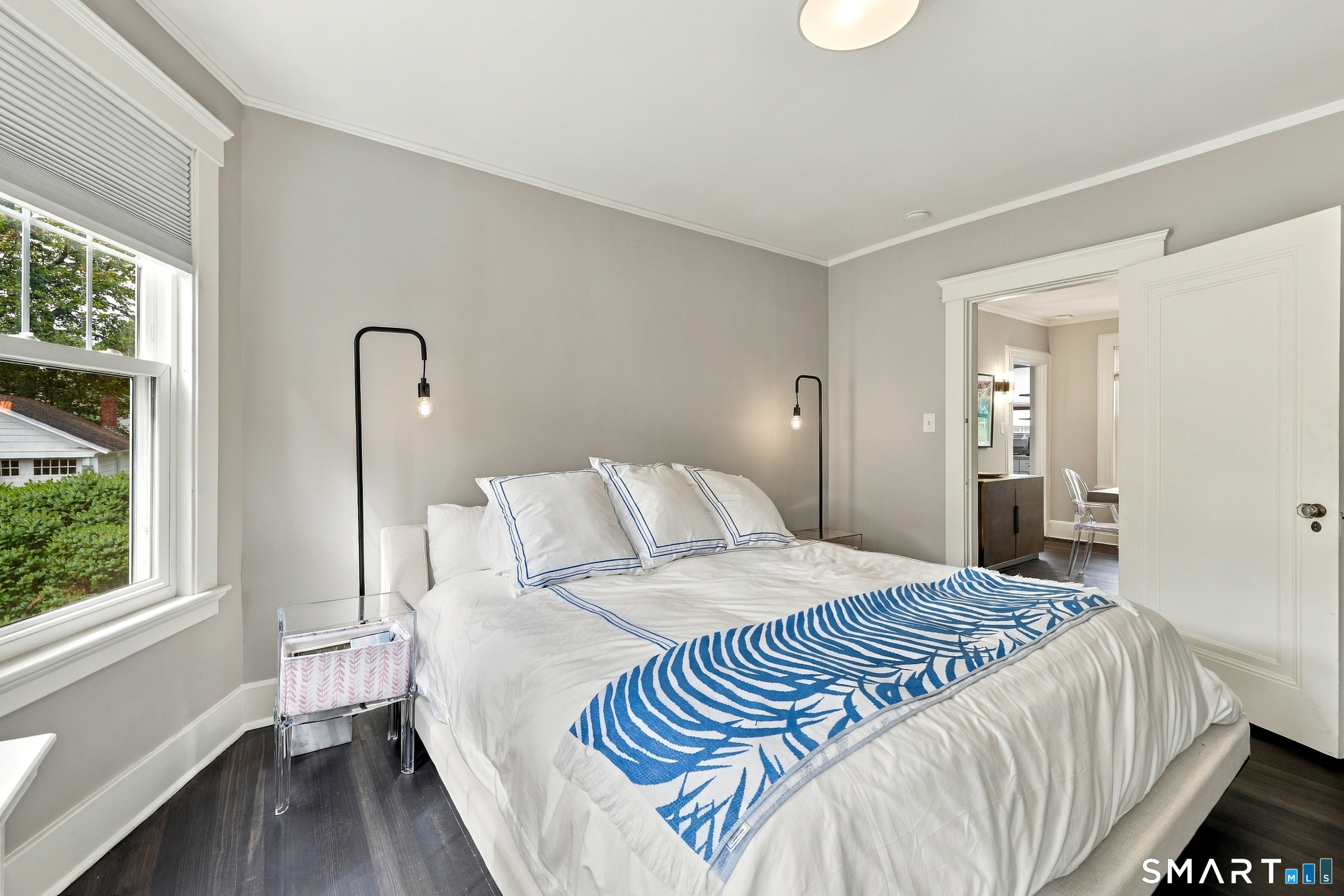 Furnished bedroom with a white bed, blue patterned throw, and large window.