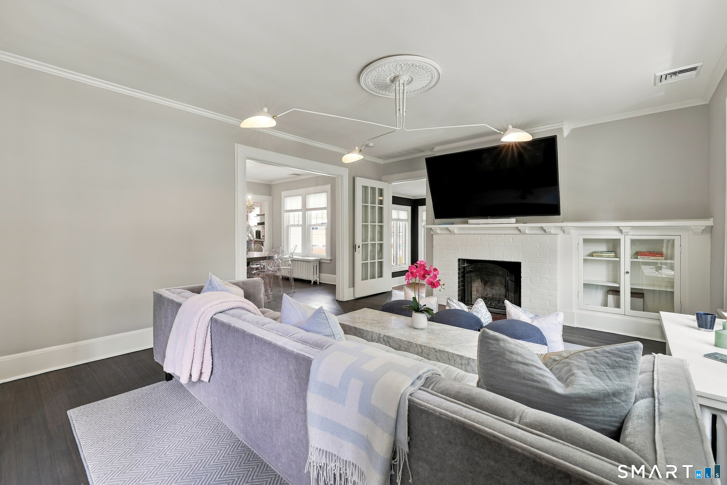Staged living room with gray sofas, white brick fireplace, and wall-mounted television.