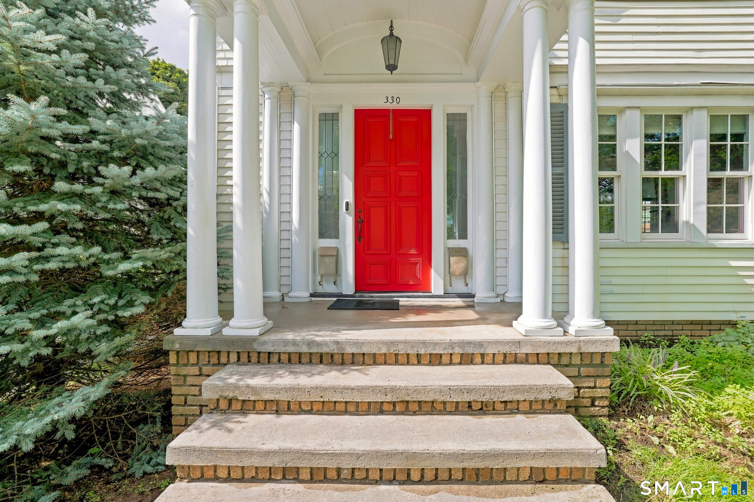 Home entrance with a bright red front door, white columns, and brick steps.