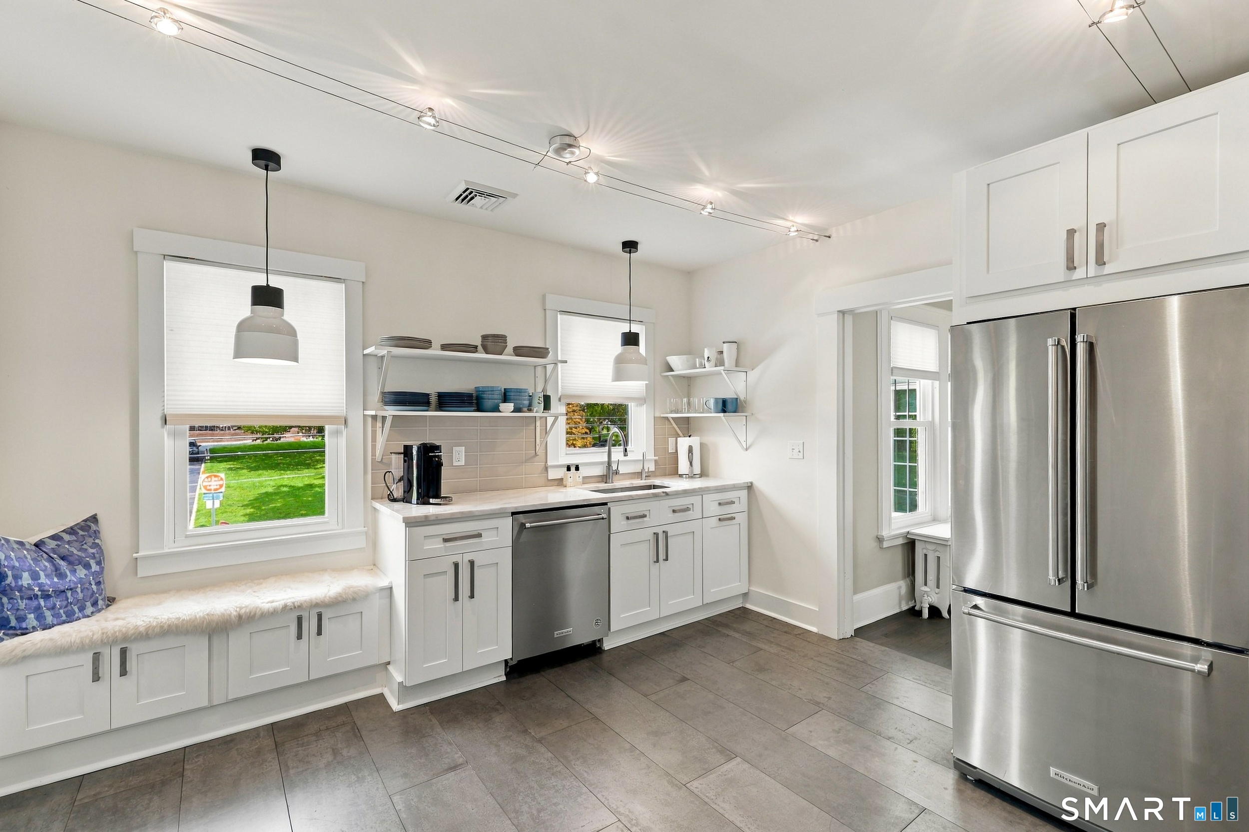 Bright kitchen with white cabinets, open shelving, stainless steel appliances, and a built-in window bench.