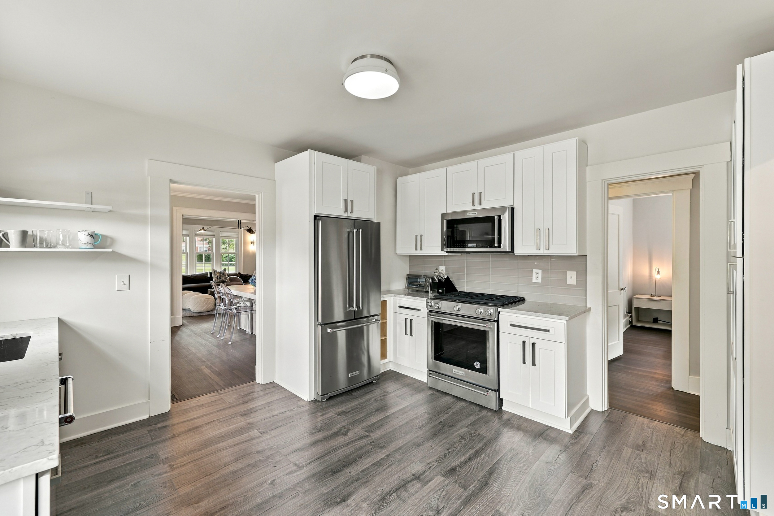 Kitchen with white cabinets, stainless steel appliances, gray tile backsplash, and wide-plank flooring.