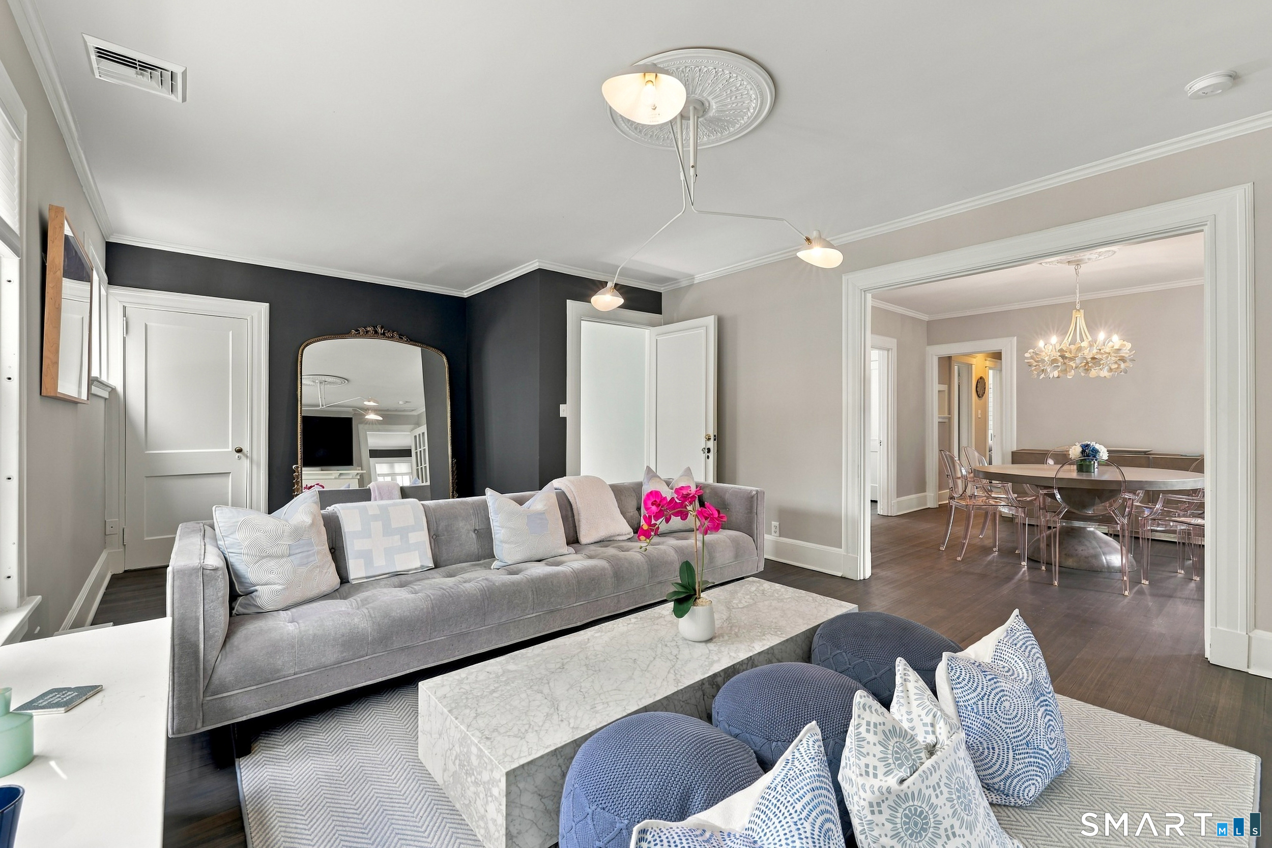 Living room with a gray sofa and marble coffee table, opening onto a chandelier-lit dining room.