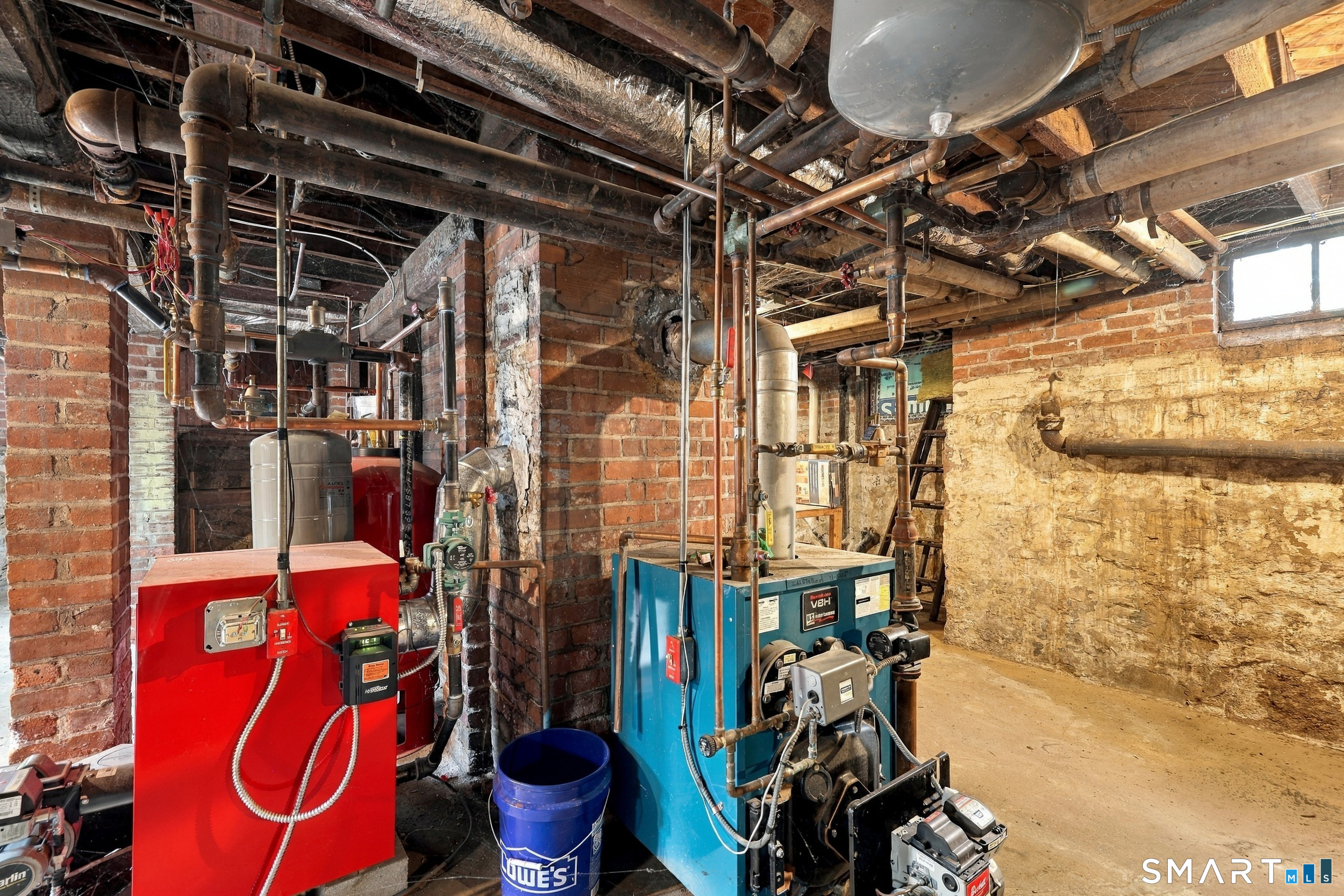 Basement mechanical room with red and blue boilers and exposed pipes.