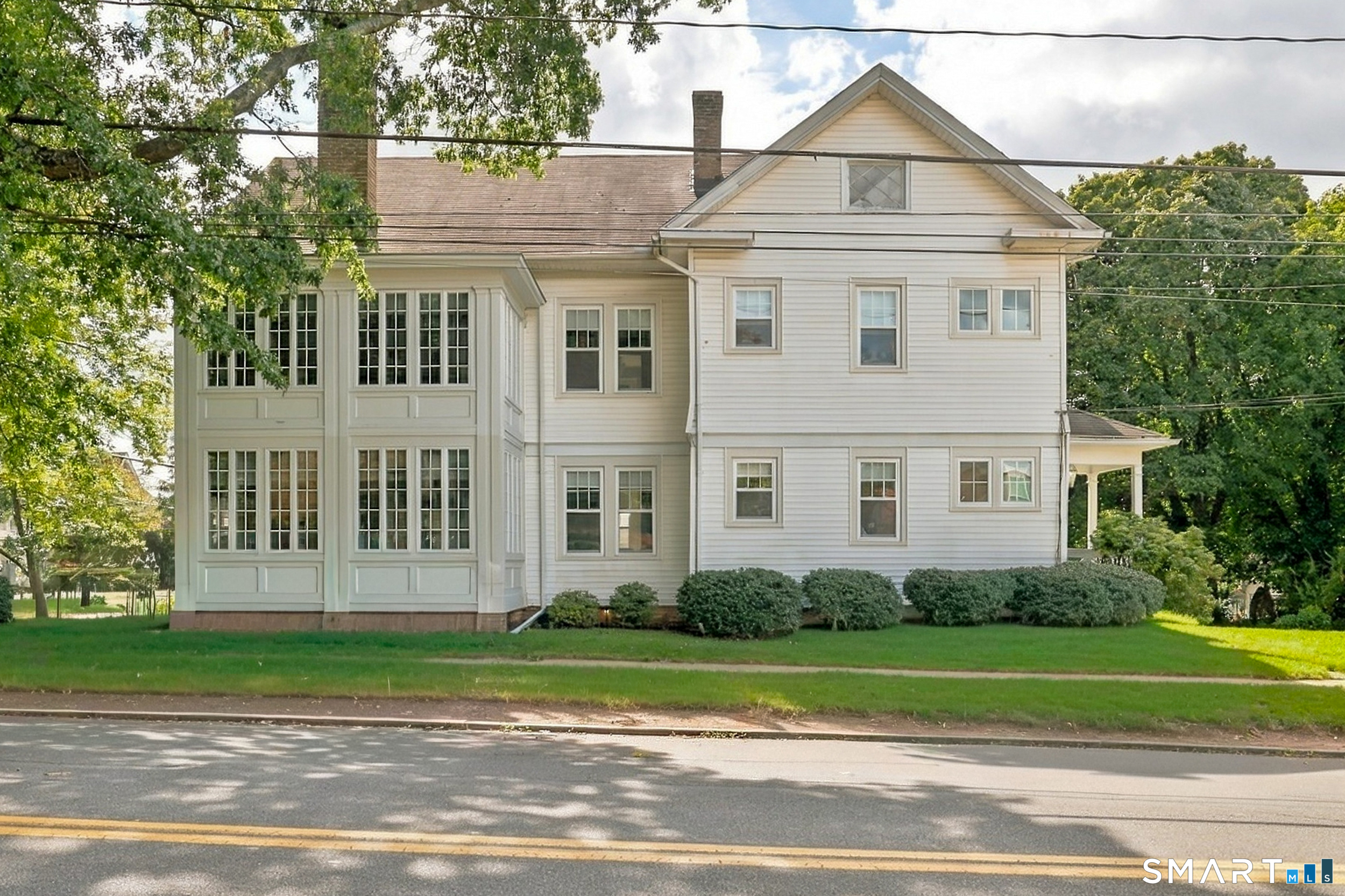 Two-story light-colored house with a prominent enclosed sunroom and rows of windows.