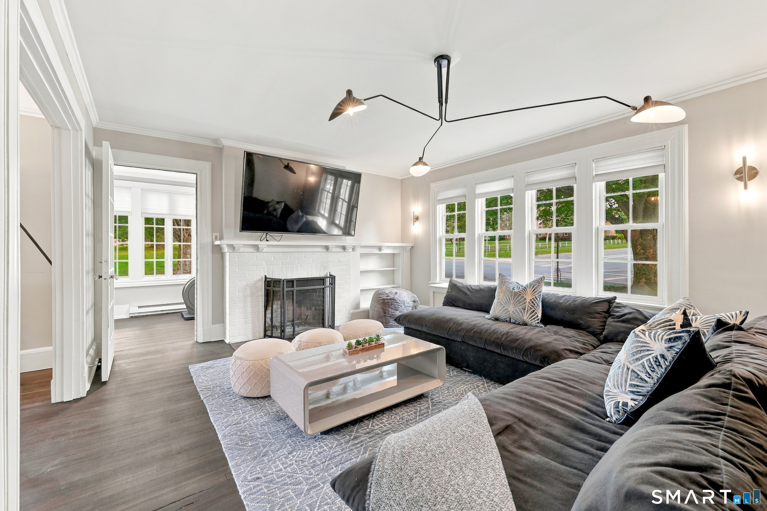 Living room with a dark sectional, white brick fireplace, mounted TV, and large street-facing windows.