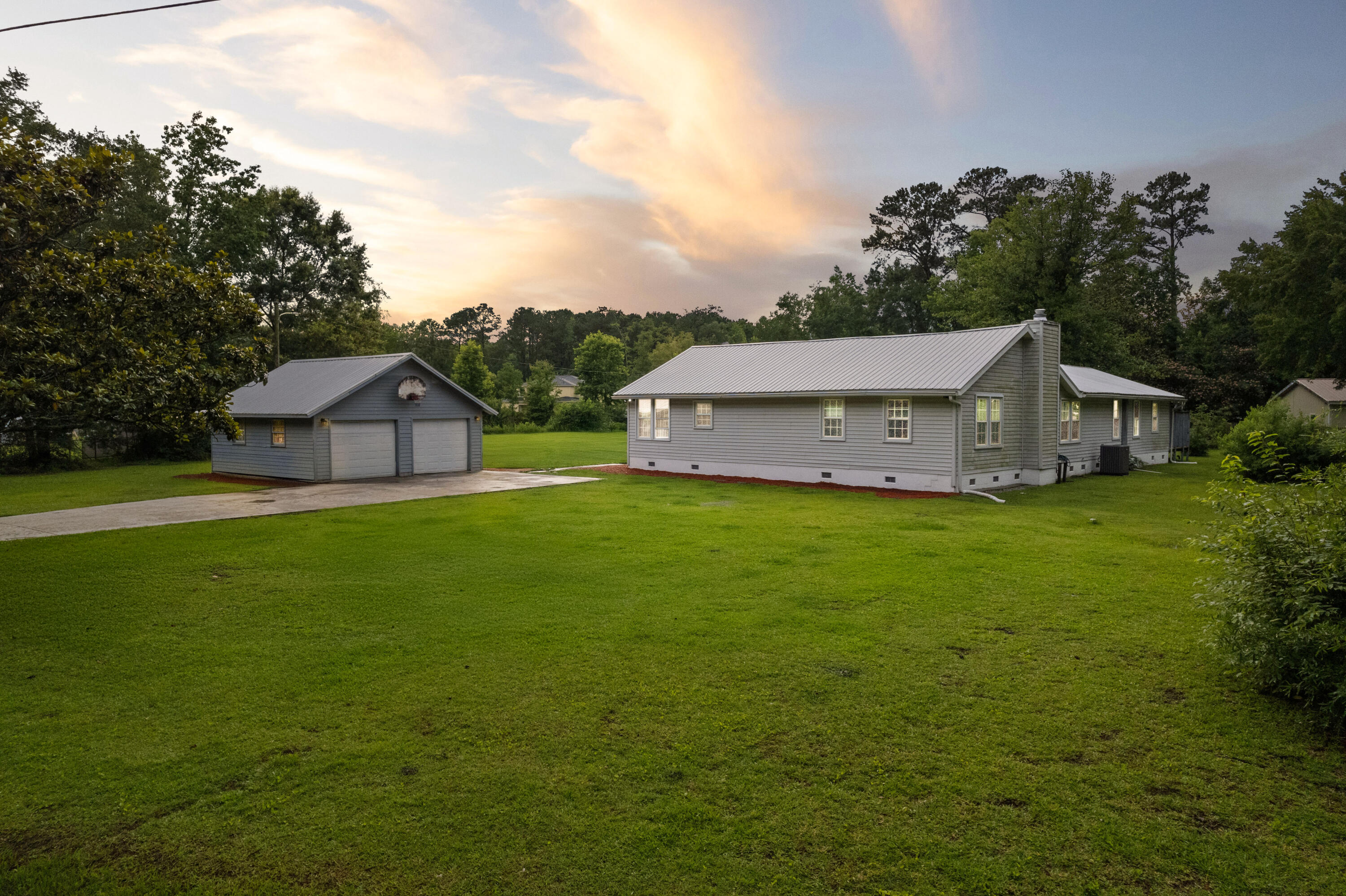 Gray single-story home and detached double garage beside a broad lawn at sunset.