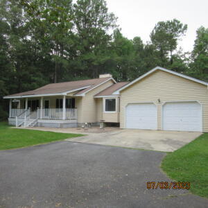 Beige single-story home with a covered porch, two garage doors, and a paved driveway.