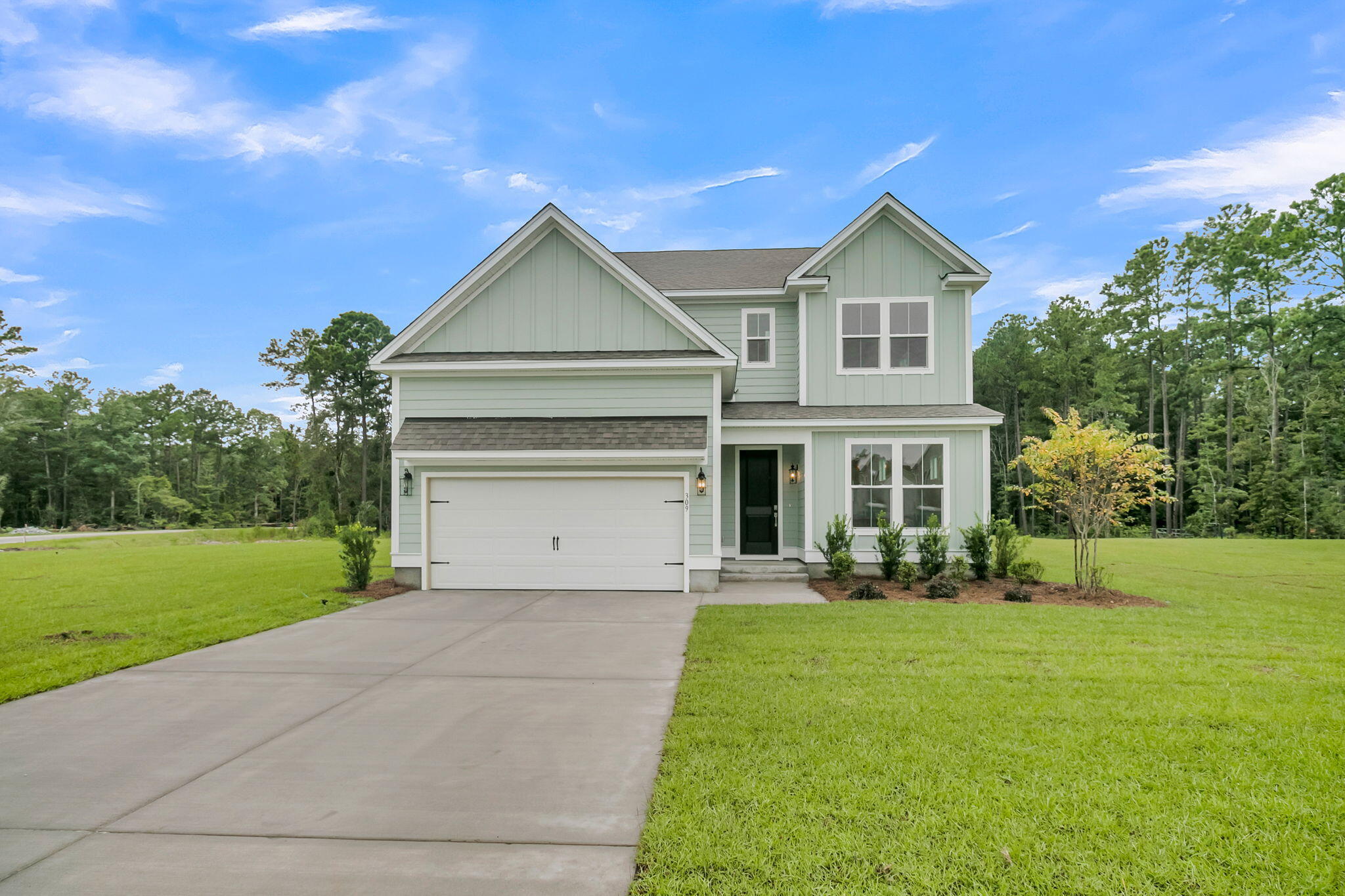 Pale green two-story home with a double garage, broad driveway, and expansive lawn.