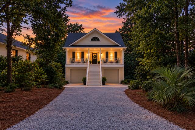 Elevated home with a lit front porch and gravel driveway at sunset.