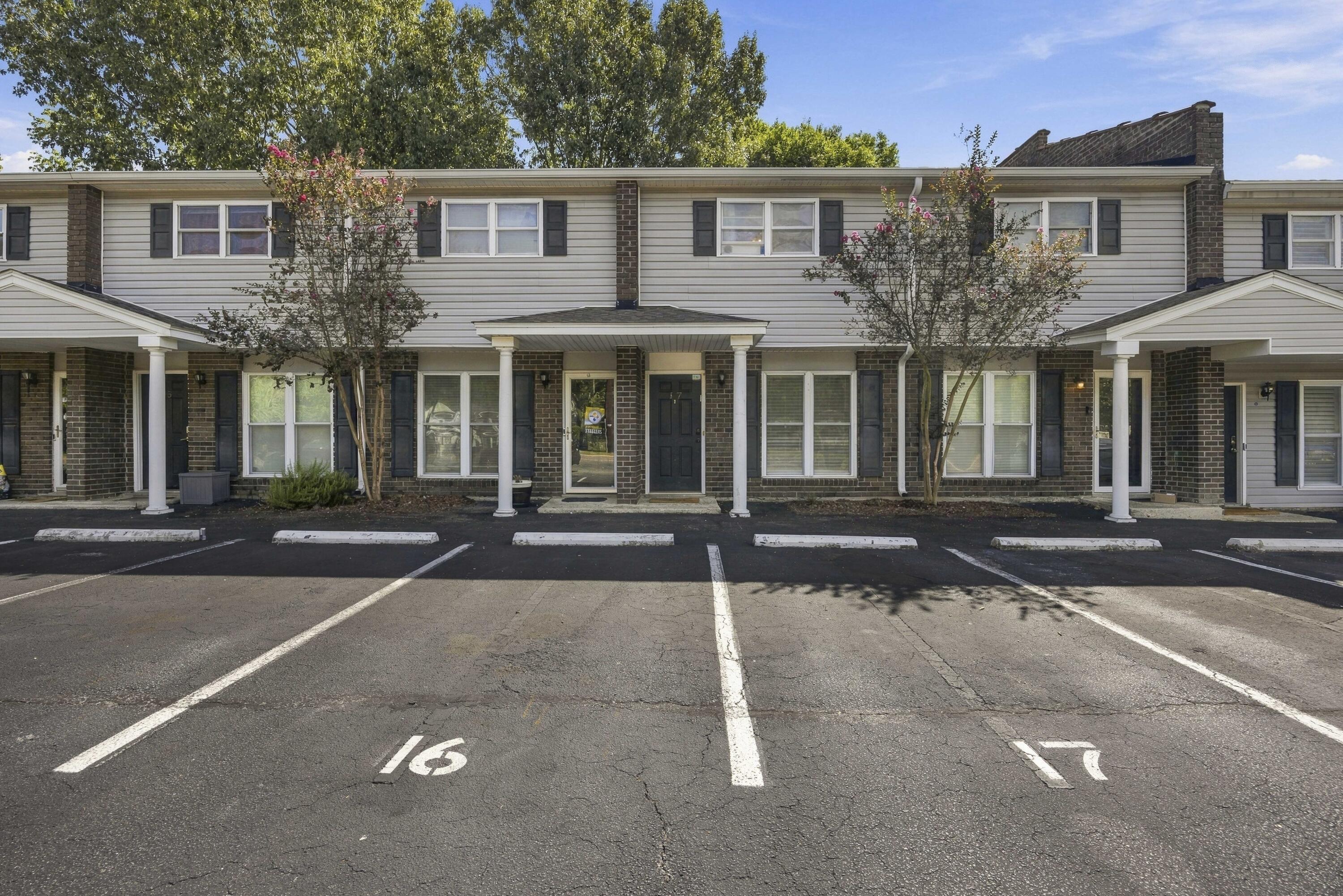 Two-story townhouse exterior with covered entrances, flowering trees, and parking spaces in front.