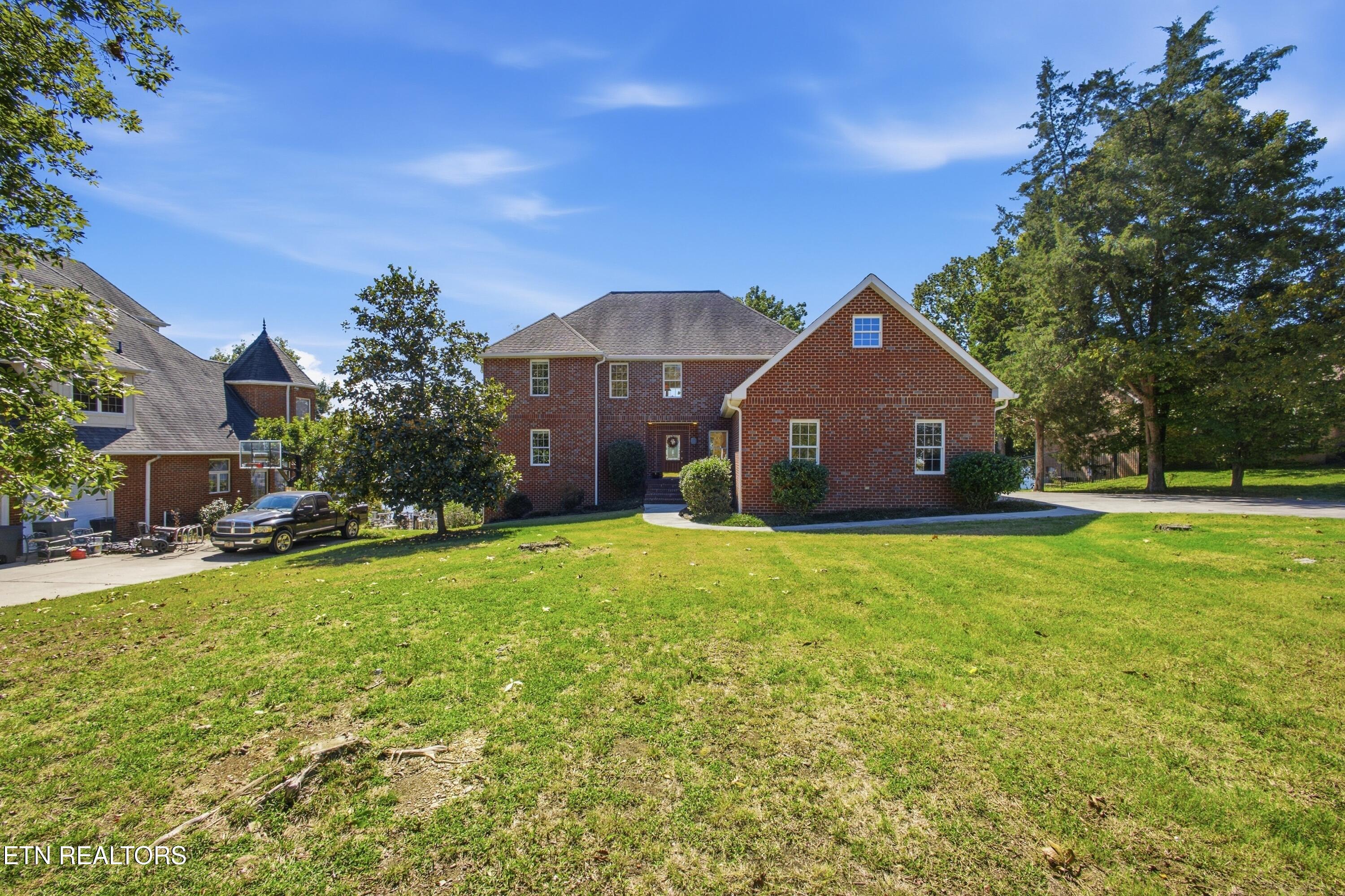 Red-brick house with a steep front gable, broad lawn, and mature trees.