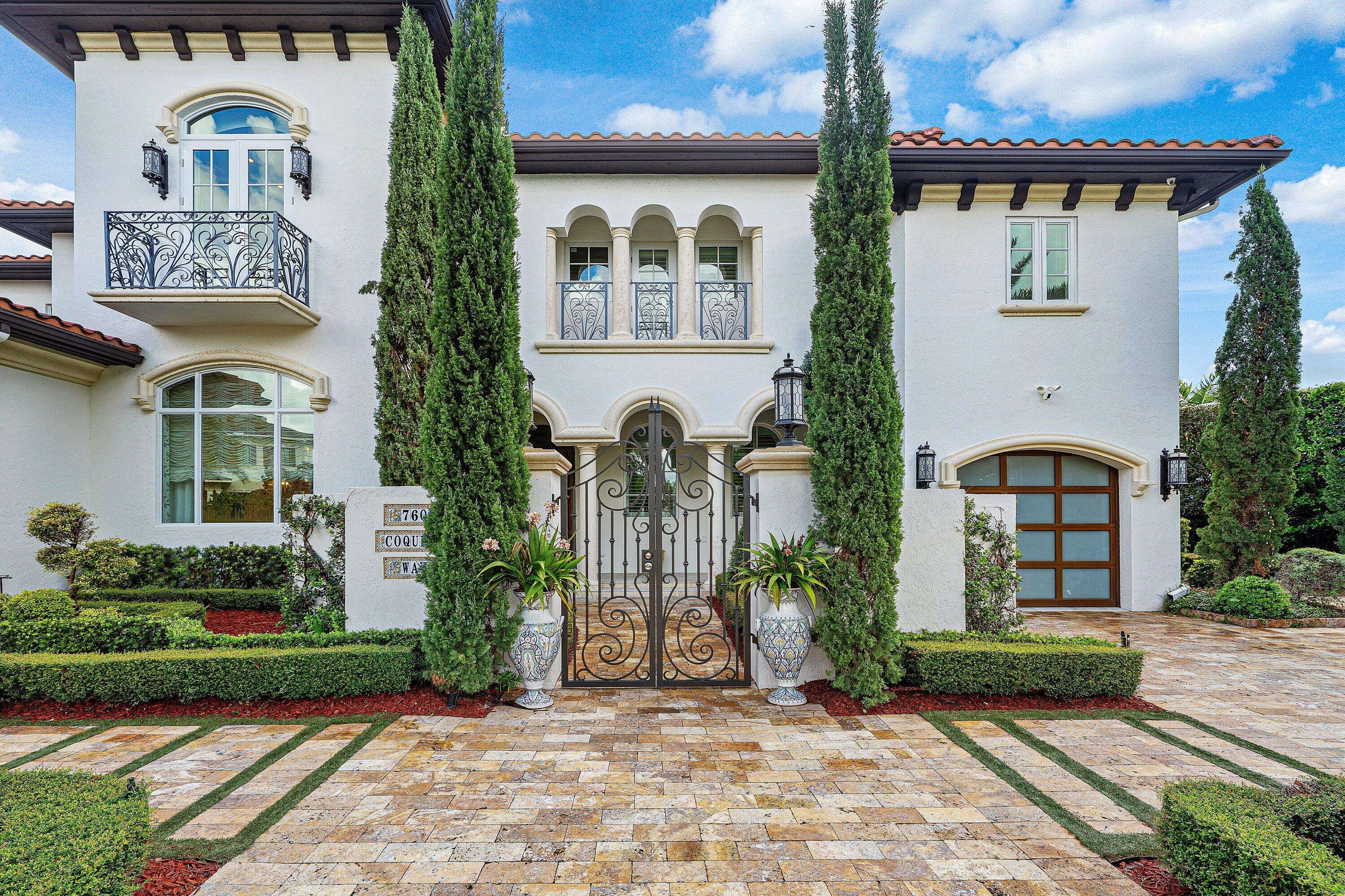 Mediterranean-style home with ornate iron entry gates, arched windows, and tall cypress trees.