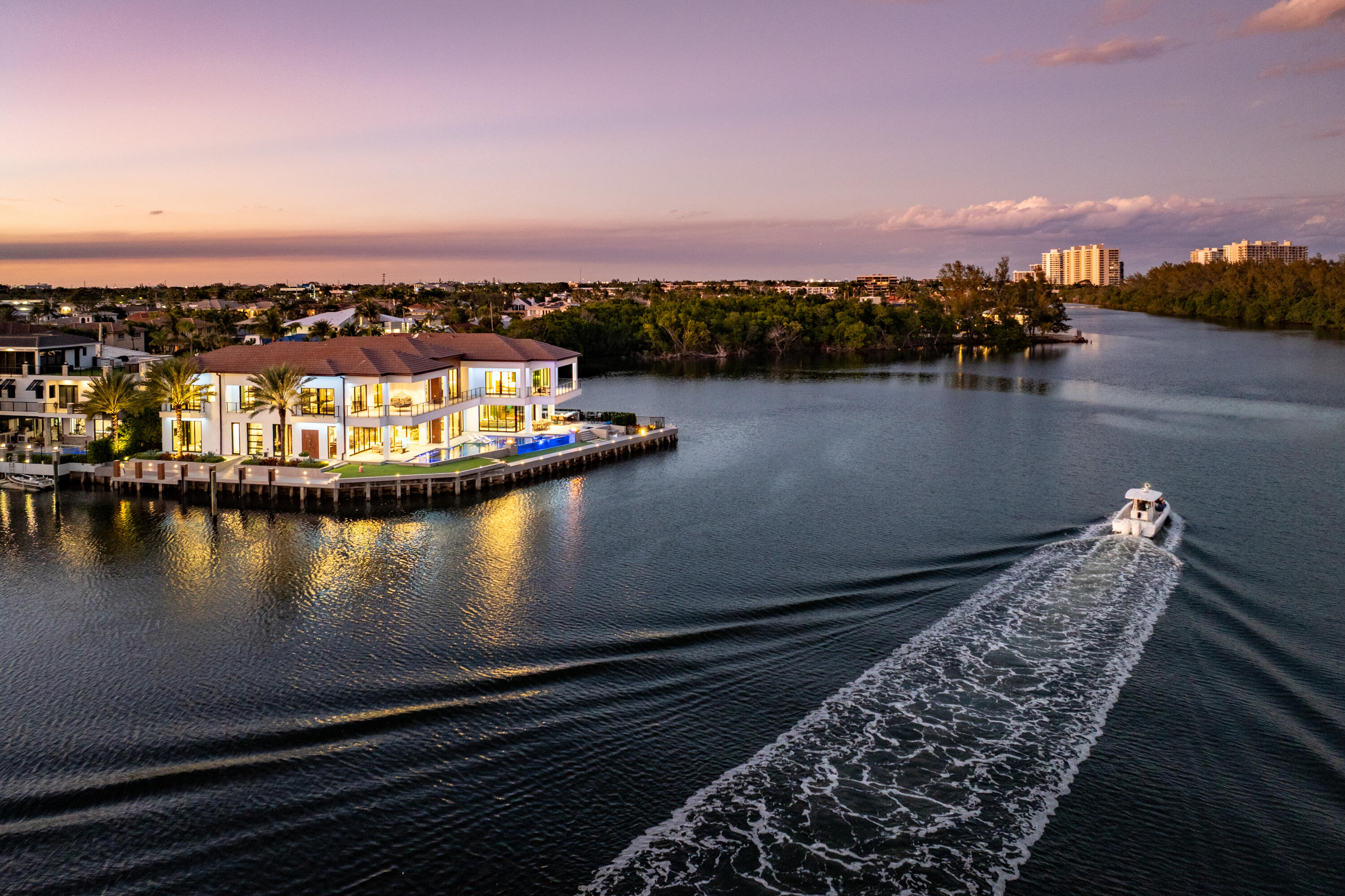 Waterfront home with a pool beside a boat wake at sunset.