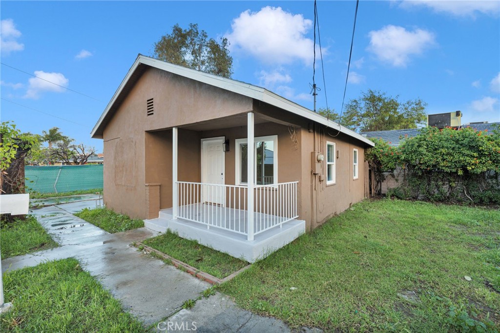 Tan stucco house with a covered porch and white railings beside a concrete walkway.