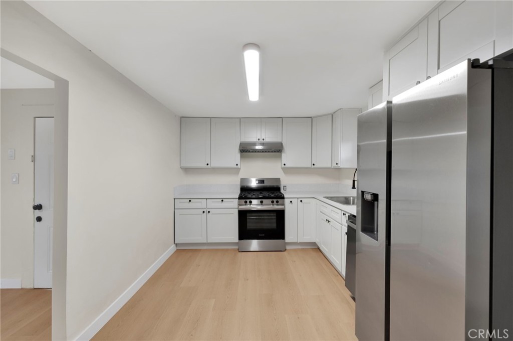 Kitchen with white cabinets, stainless steel appliances, and light wood flooring.