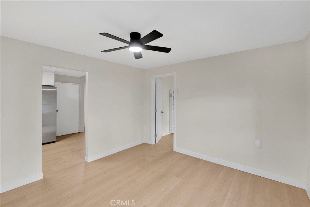 Empty room with pale wood flooring and a black ceiling fan, opening to the kitchen.