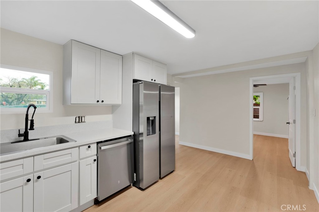 Kitchen with white cabinetry, stainless steel appliances, and light wood flooring.