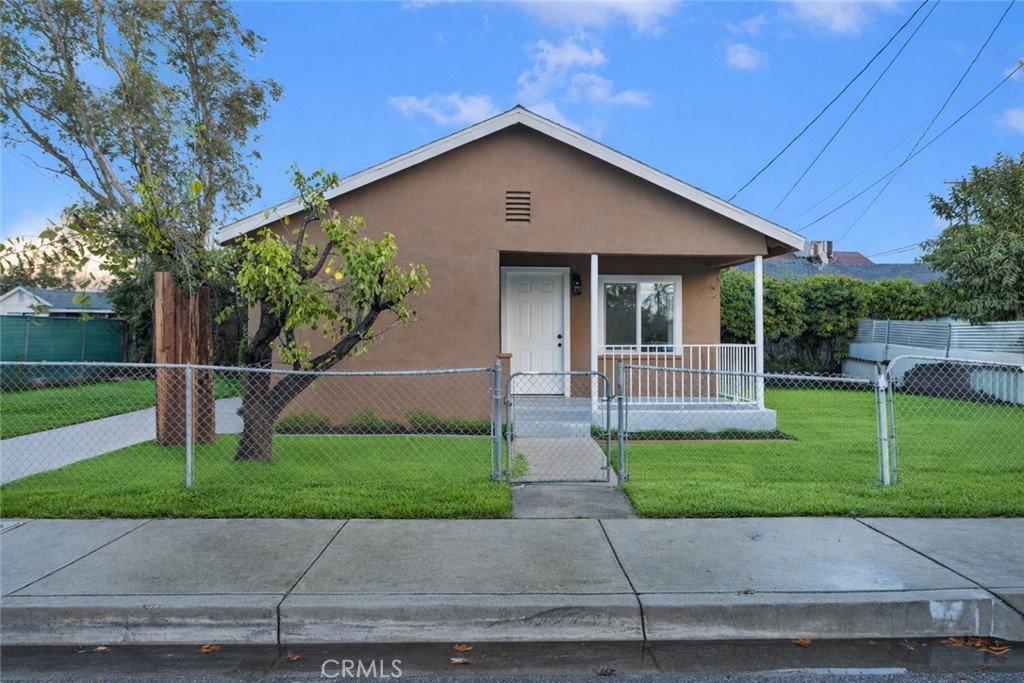 Brown single-story house with a covered porch, chain-link fence, and green front lawn.