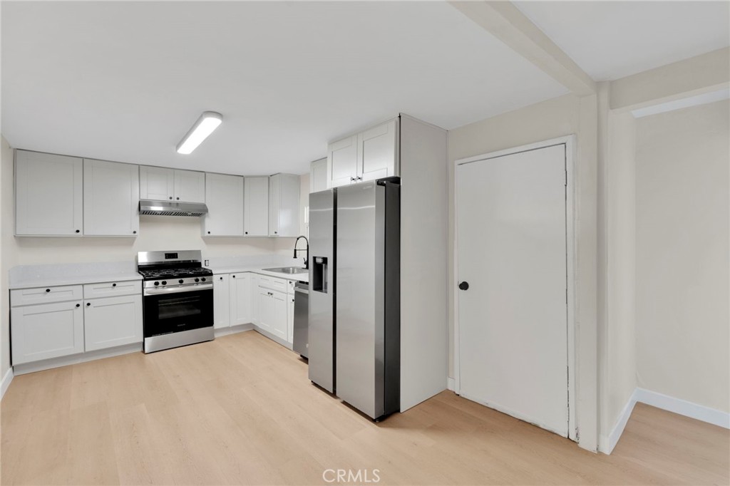 Vacant kitchen with white cabinets, stainless steel appliances, and pale wood flooring.