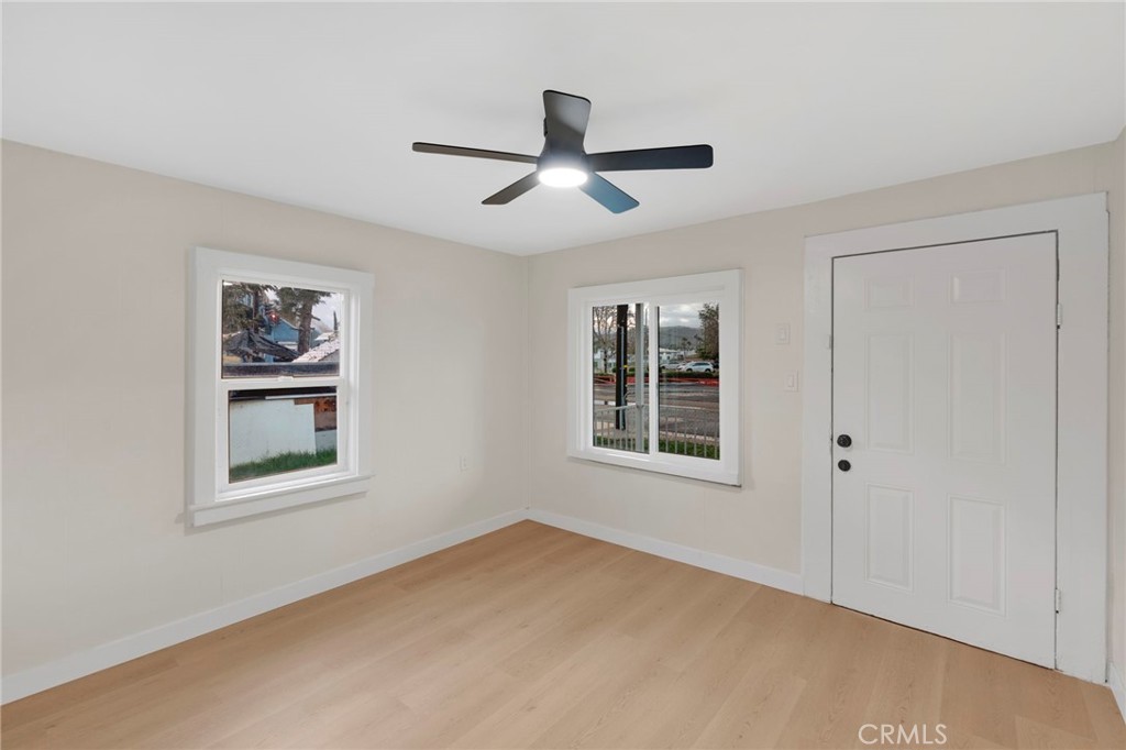 Empty room with light wood flooring, two windows, a white entry door, and a ceiling fan.