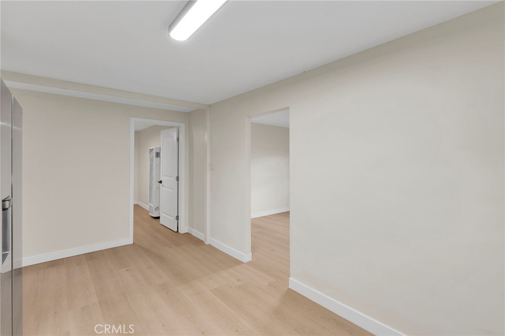 Empty room with pale wood floors, adjoining doorways, and a ceiling light.