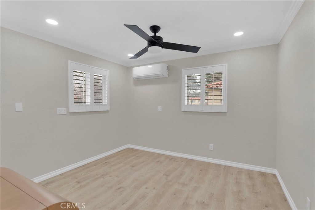 Bedroom with wood-look flooring, shuttered windows, a black ceiling fan, and a wall-mounted air conditioner.