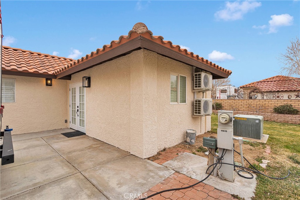 Single-story stucco home with a tile roof, covered patio, and exterior air-conditioning units.