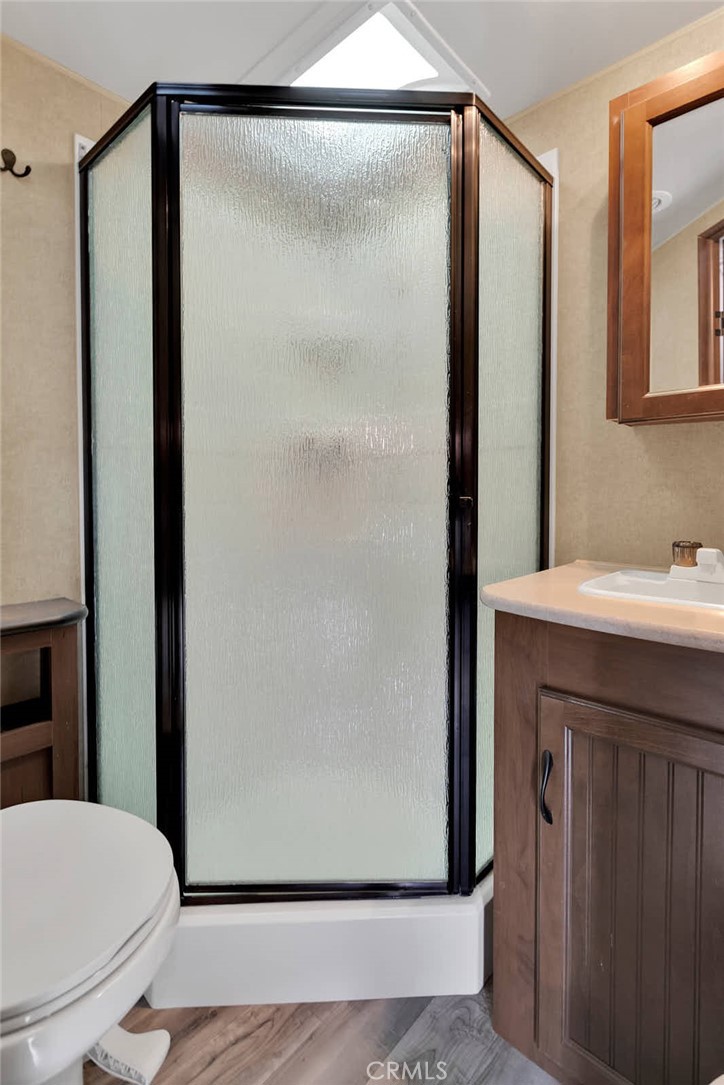 Bathroom with a textured-glass corner shower, wood vanity, and skylight.