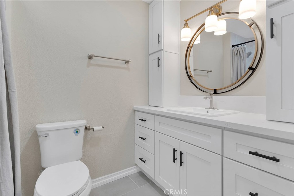 Bathroom with white vanity, round gold-framed mirror, built-in cabinets, and toilet.