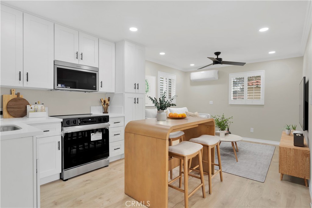 Open-plan kitchen with white cabinets, stainless appliances, and a light wood island with stools.