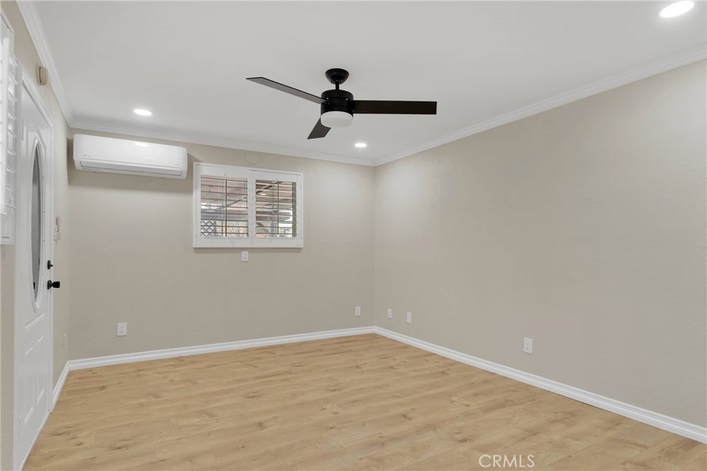 Empty room with wood-look flooring, a ceiling fan, shuttered window, and wall-mounted air conditioner.