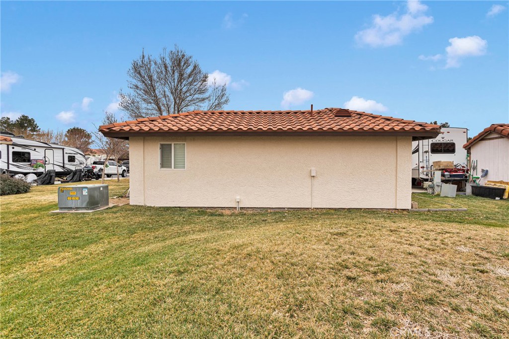 Side of a stucco house with a terracotta tile roof and broad lawn.